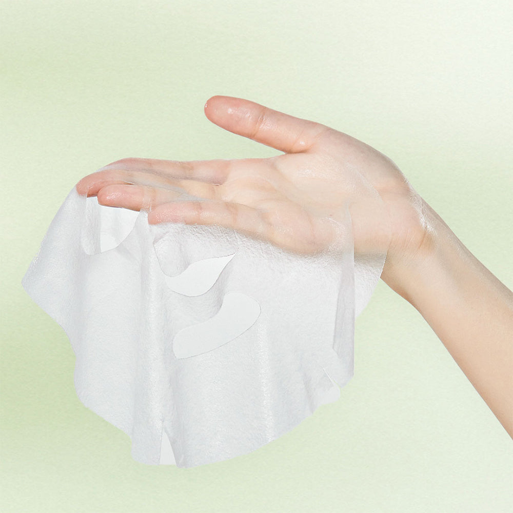 Hand holding an unfolded Mixsoon Centella sheet mask against a green background